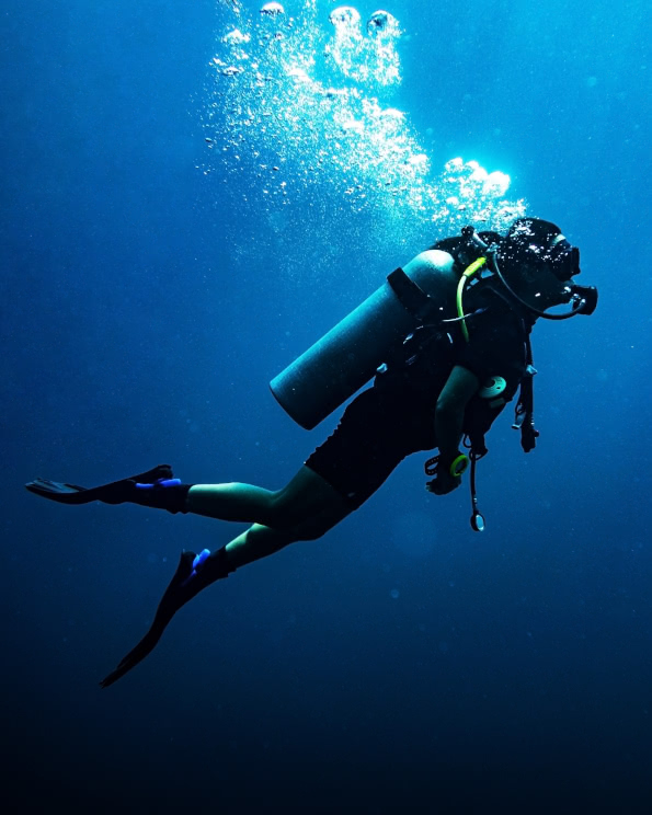 Scuba diver swimming alone in deep blue water with air bubbles rising to the surface